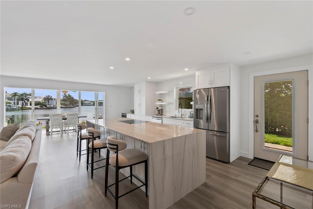 Image 4: Open-concept living area featuring an expansive kitchen island with a waterfall countertop, integrated stainless steel appliances, and wood-finish flooring