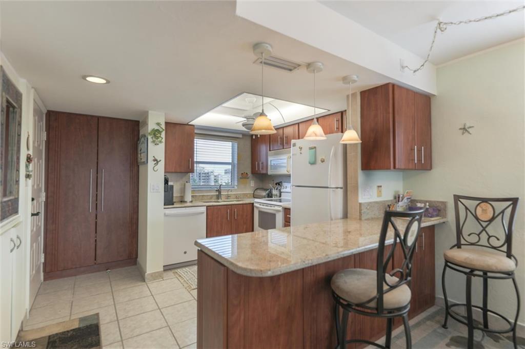 Image 4: Kitchen featuring hanging light fixtures, white appliances, kitchen peninsula, sink, and light tile flooring