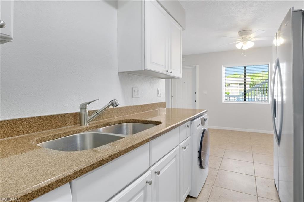 Image 2: Kitchen with light tile patterned floors, washer / dryer, freestanding refrigerator, a sink, and white cabinetry