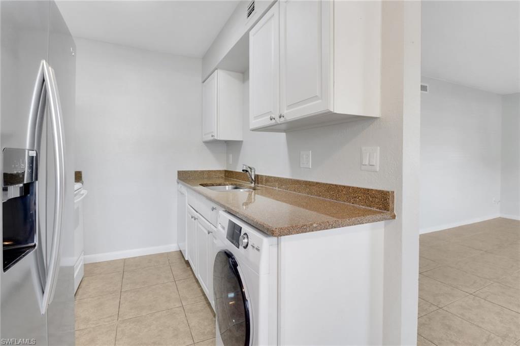 Image 3: Kitchen with dark stone countertops, washer / dryer, stainless steel refrigerator with ice dispenser, white cabinetry, and a sink