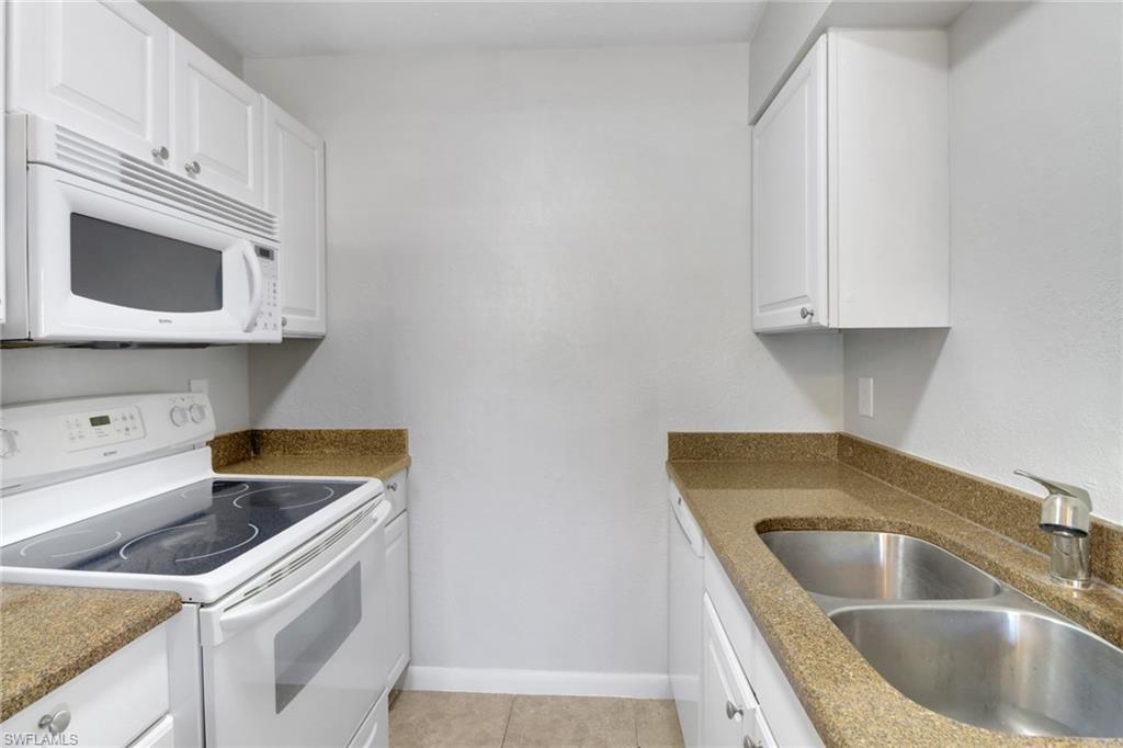 Image 4: Kitchen featuring a sink, white cabinetry, white appliances, light tile patterned flooring, and baseboards