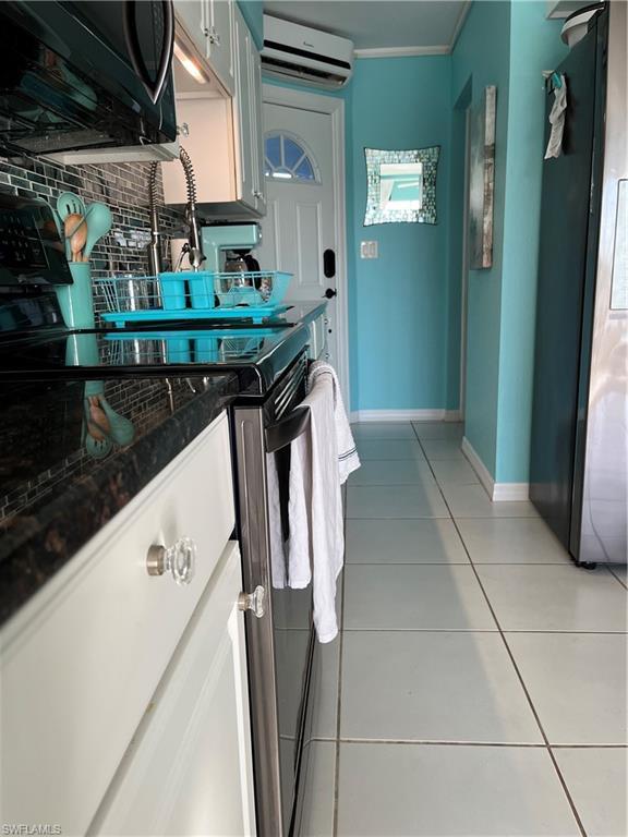 Image 3: Kitchen with an AC split unit,  range, light tile patterned floors, decorative backsplash, and baseboards