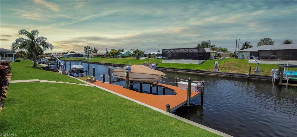 Image 3: Waterfront property featuring a private boat dock with lift, lush green lawn, and mature palm trees