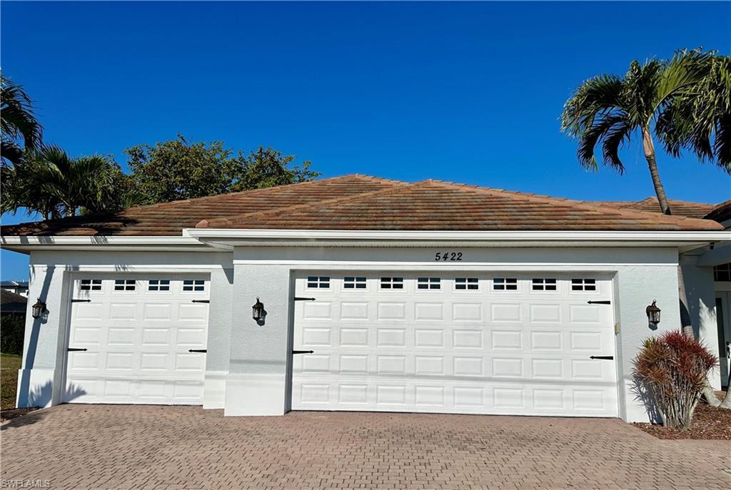 Image 2: View of Newly Painted Three Car Garage with Three Car Paver Driveway and Exterior Outdoor Garage Sconce Illumination.
