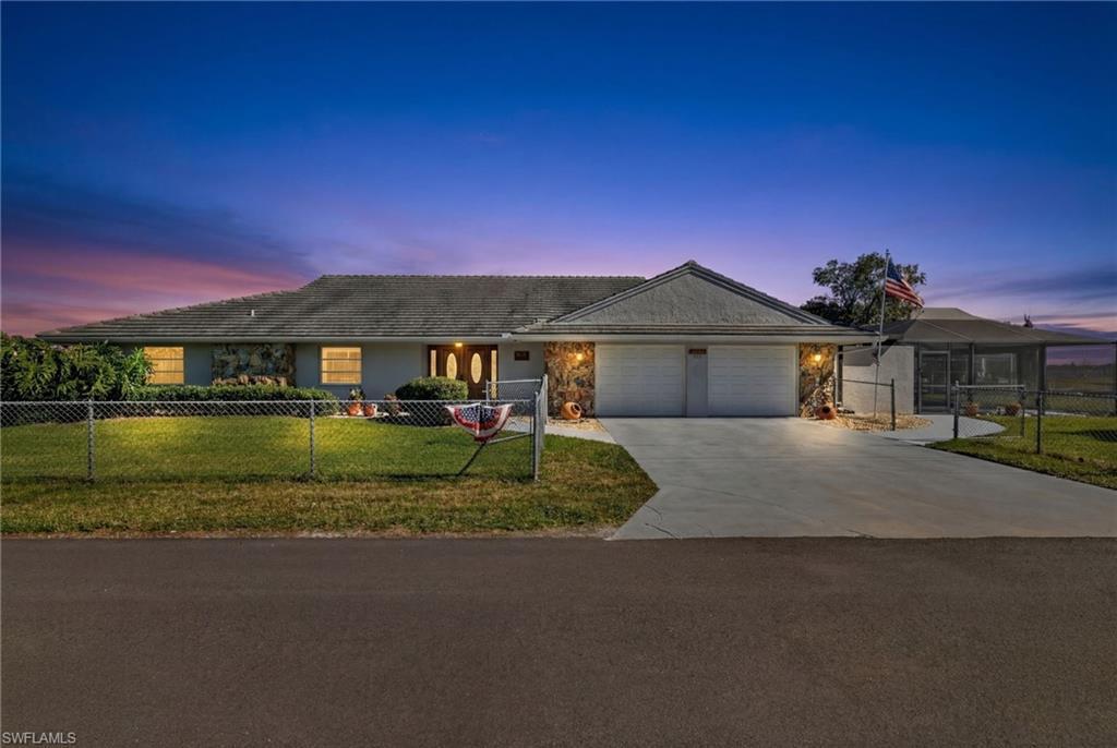 Image 1: Ranch-style home with a fenced front yard, driveway, an attached garage, and stone siding