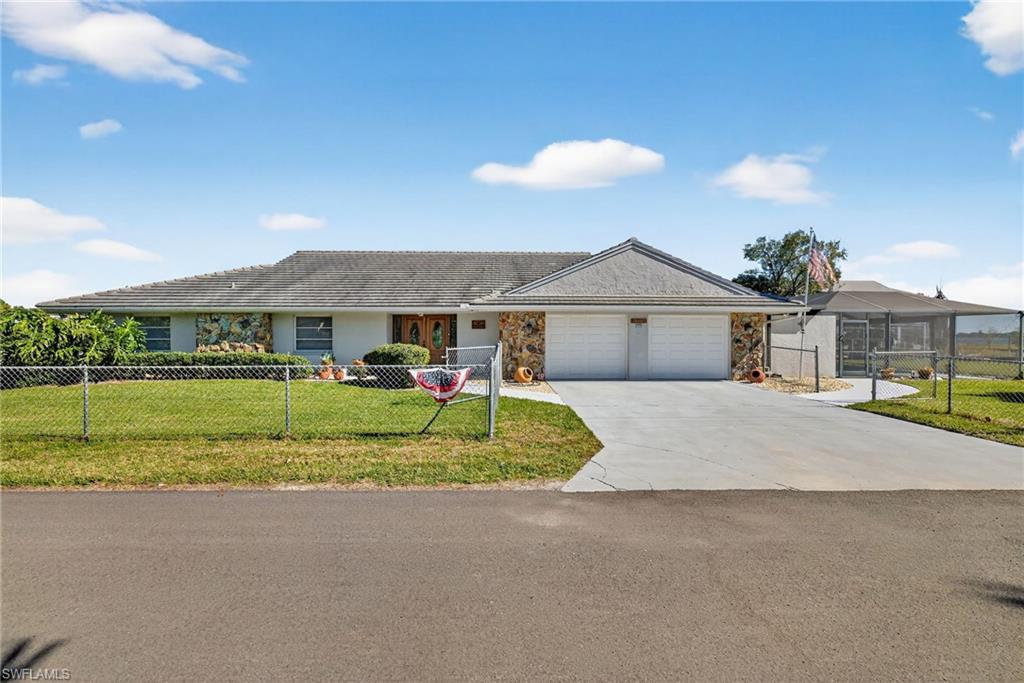 Image 2: Ranch-style house with a fenced front yard, stone siding, concrete driveway, and a garage