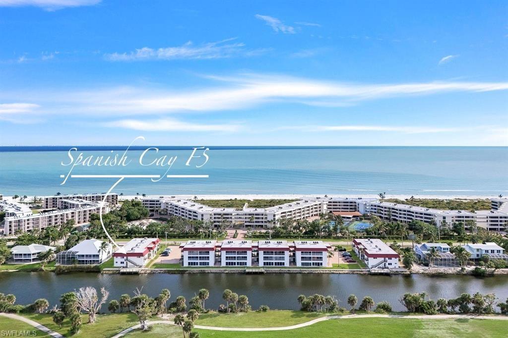 Image 1: Waterfront condominium community with direct beach access, featuring multiple residential buildings, lush landscaping, and recreational amenities including a tennis court