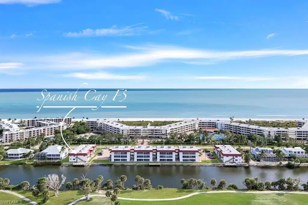 Image 1: Waterfront condominium community with direct beach access, featuring multiple residential buildings, lush landscaping, and recreational amenities including a tennis court