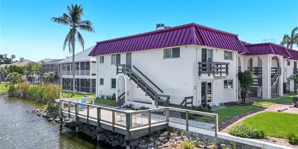 Image 2: Waterfront property featuring a private wood dock with metal railings, white exterior, purple metal roof, and multiple balconies
