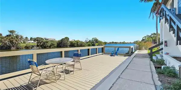Image 3: Waterfront deck featuring a composite surface, white railing with mesh infill, and a palm tree