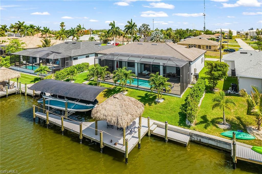 Image 1: Waterfront property featuring a private dock with a covered boat lift, an additional dock with a tiki hut, a screened-in lanai, and an in-ground swimming pool