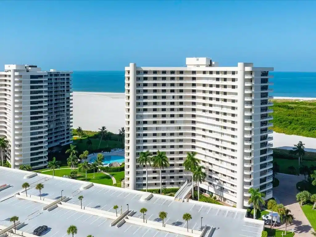 Image 1: High-rise coastal building with multiple private balconies, expansive parking structure, direct beach access, and a resort-style pool with surrounding landscaping