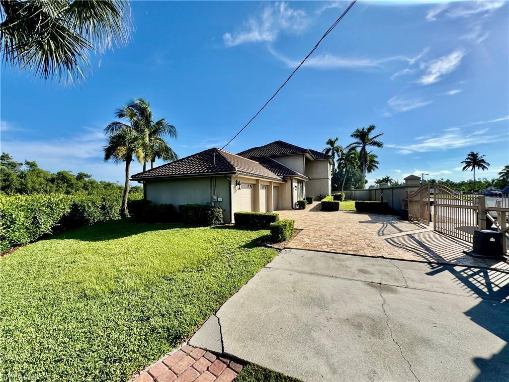 Image 2: View of side of home with decorative driveway, a garage, a gate, stucco siding, and a tile roof