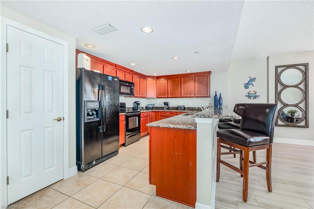 Image 4: Kitchen with black appliances, a kitchen bar, a peninsula, light stone countertops, and a textured ceiling