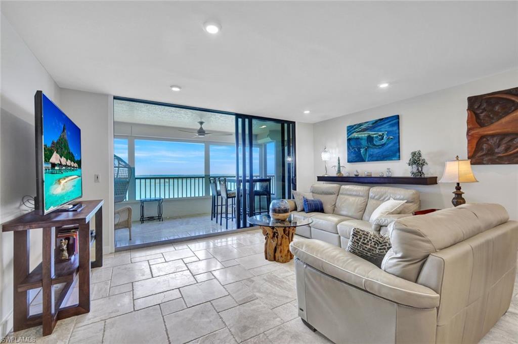 Image 3: Living room with a ceiling fan, expansive windows, and stone tile flooring