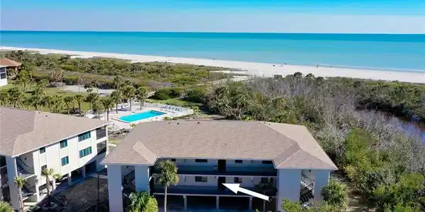 Image 2: Coastal residential building featuring multiple levels and balconies, with a sandy beach and turquoise ocean visible in the background