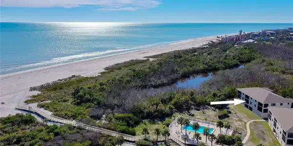 Image 3: Extensive beachfront property featuring a multi-story building, an outdoor swimming pool, and a boardwalk accessing a wide sandy beach