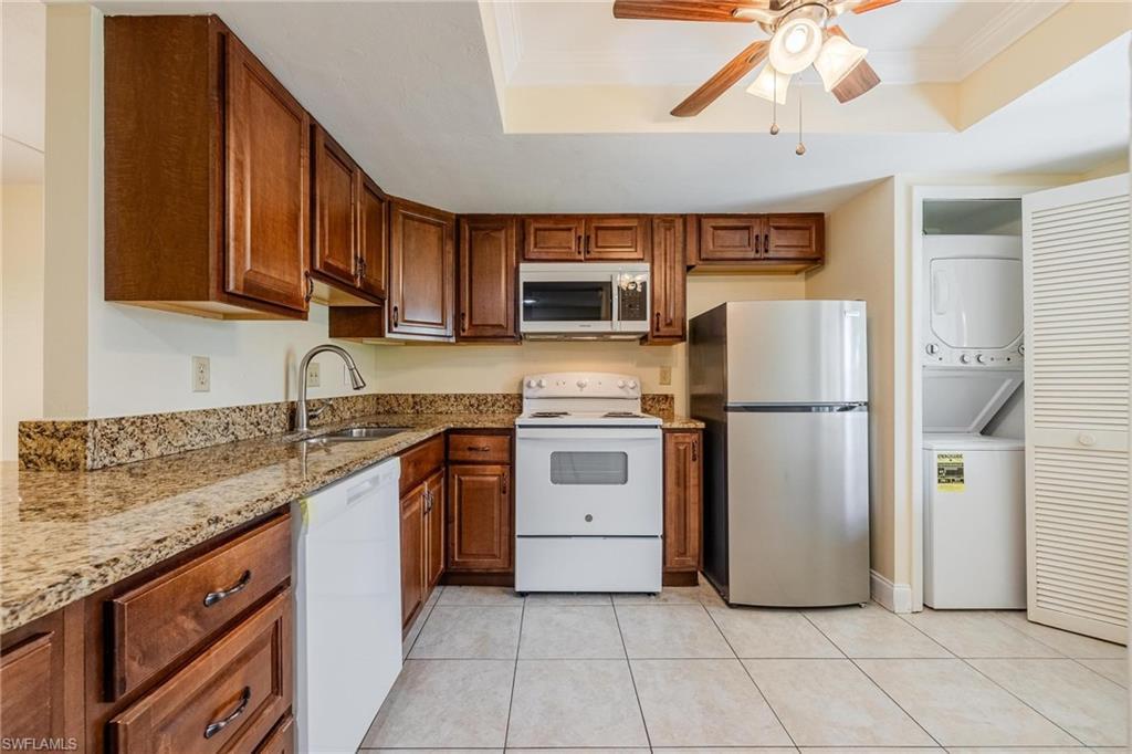 Image 3: Kitchen with granite counters, dark wood cabinets, stacked washer / dryer, crown molding, and a tray ceiling