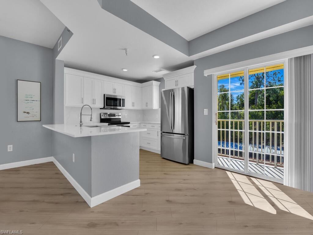 Image 1: Kitchen featuring stainless steel appliances, white cabinets, a peninsula, light wood-style floors, and light stone counters