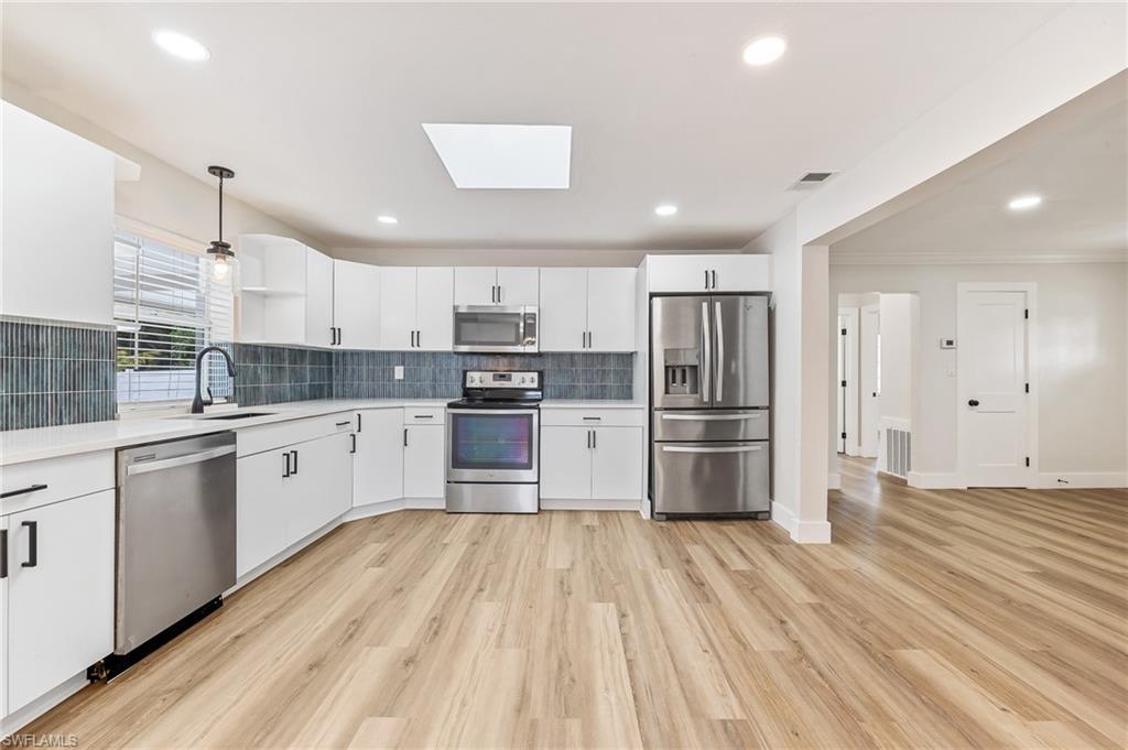 Image 4: Kitchen with appliances with stainless steel finishes, white cabinets, backsplash, a skylight, and decorative light fixtures