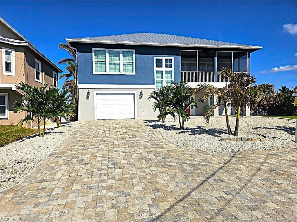 Image 2: Coastal home featuring an attached garage, stucco siding, a sunroom, decorative driveway, and metal roof