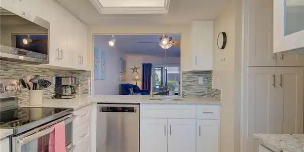 Image 2: Kitchen featuring stainless steel appliances, white cabinetry, light tile patterned floors, and backsplash