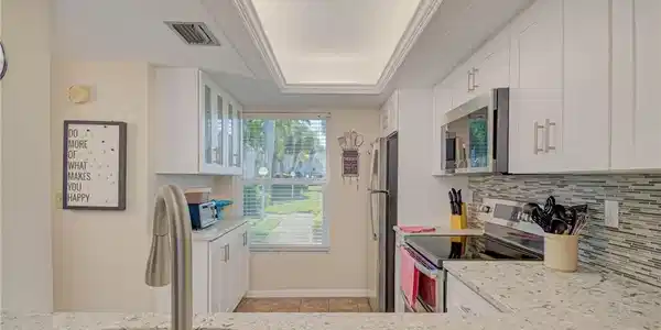 Image 4: Kitchen with white cabinetry, stainless steel appliances, light stone counters, a tray ceiling, and decorative backsplash