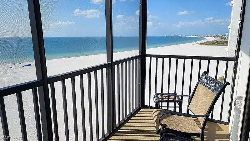 Image 1: Private direct beachfront corner/end unit balcony showcasing sweeping Gulf views of Fort Myers Beach to Sanibel, the perfect setting for morning coffee or sunset relaxation. Comfortable chairs invite you to unwind while enjoying the sights and sounds of the gulf beach.