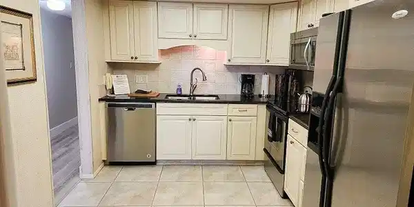 Image 4: Kitchen with stainless steel appliances, decorative backsplash, white cabinetry, dark stone counters, and light tile patterned floors