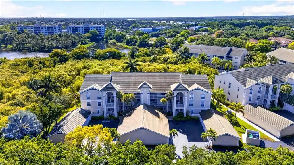 Image 1: Multi-story building featuring light-colored siding, multiple balconies, and gabled rooflines, surrounded by extensive natural landscaping