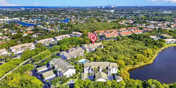 Image 2: Aerial perspective featuring a community with multiple residential buildings, lush green landscaping, a prominent body of water, and distant urban skyline