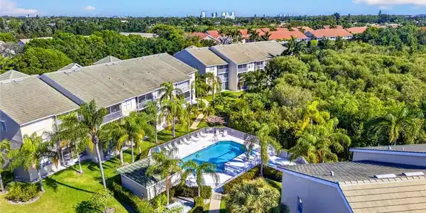 Image 3: Community pool with surrounding lounge area, multiple multi-story residential buildings with balconies, mature palm trees, and manicured green spaces