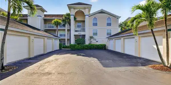 Image 4: Exterior view of a multi-story building featuring stucco siding, multiple balconies with white railings, and a central arched entrance