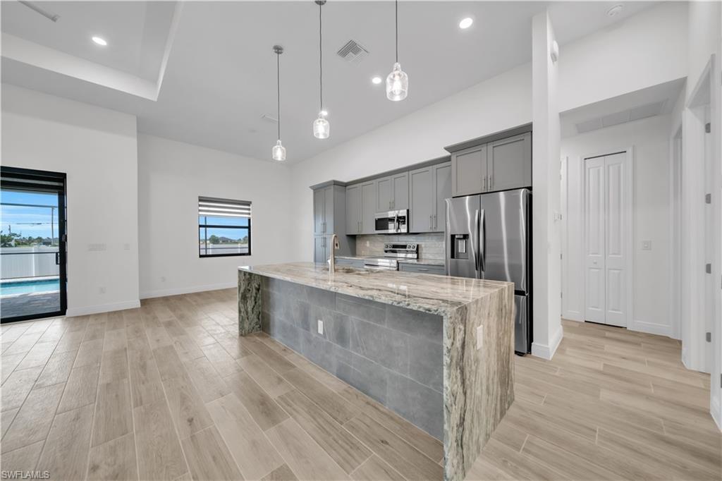 Image 3: Kitchen featuring gray cabinetry, decorative light fixtures, stainless steel appliances, wood tiled floors, and light stone countertops