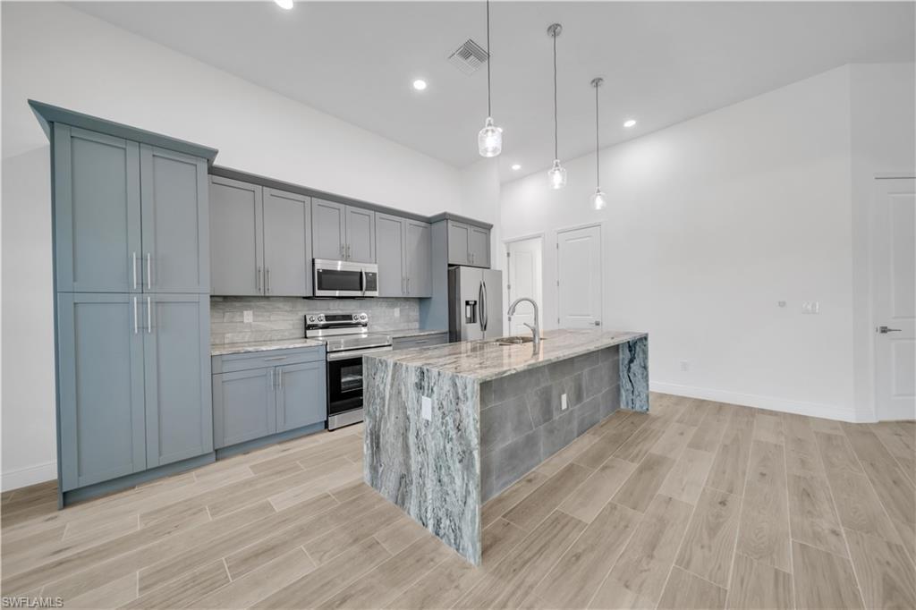 Image 4: Kitchen with wood finish floors, stainless steel appliances, hanging light fixtures, and light stone counters
