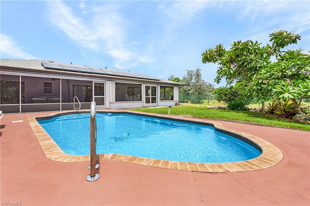 Image 1: Freeform swimming pool with a red-toned concrete deck, brick-patterned coping, and a stainless steel handrail