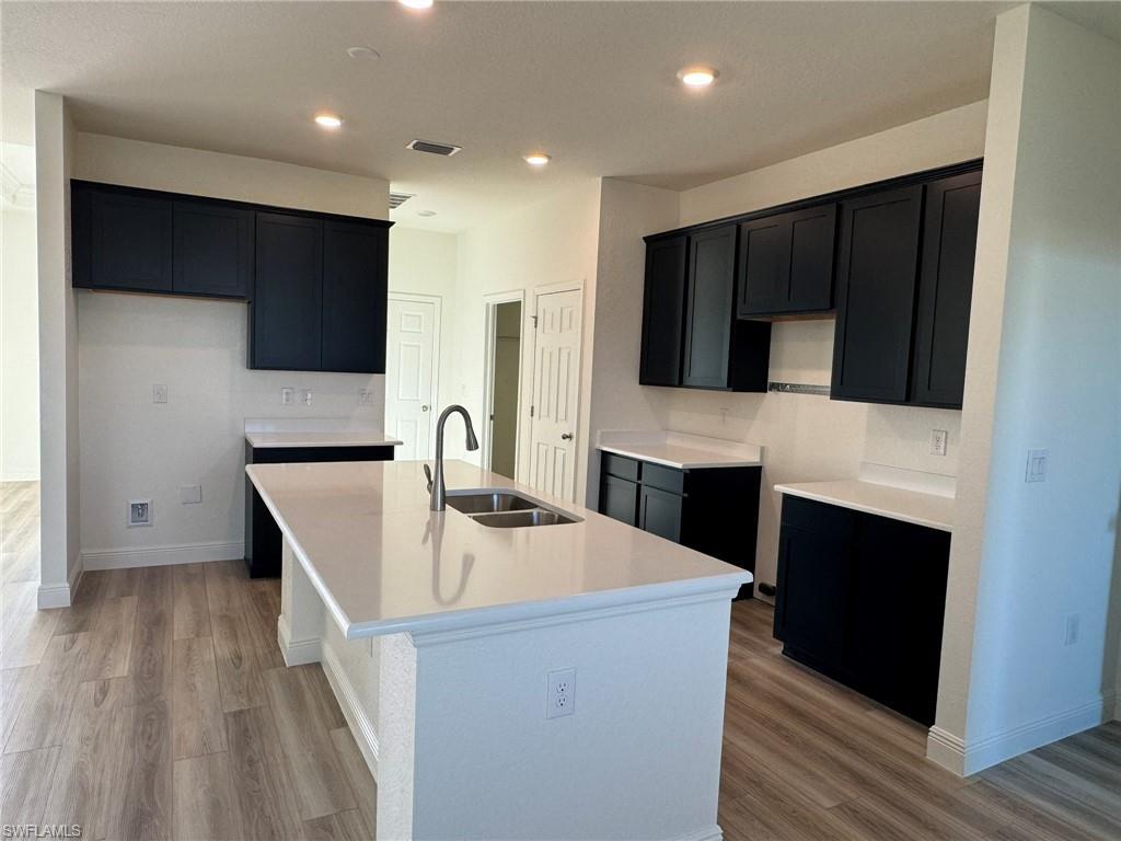 Image 4: Kitchen featuring a sink, an island with sink, light wood-style floors, dark cabinets, and recessed lighting