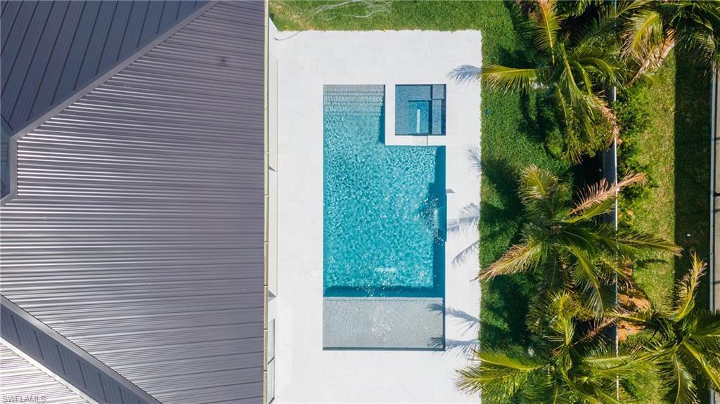 Image 3: Aerial view showcasing a pristine swimming pool, surrounding patio area, and neatly maintained green lawn with palm trees