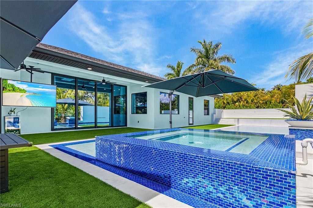 Image 3: Outdoor space featuring a blue mosaic tiled spa with integrated pool, artificial turf, and a covered patio with an outdoor television