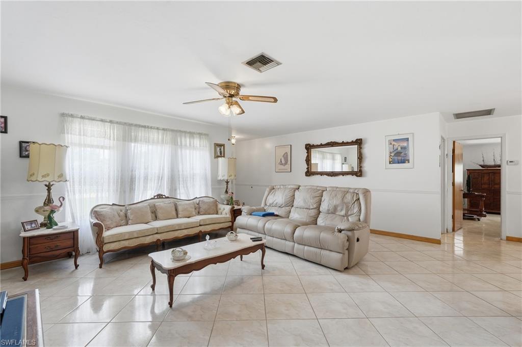 Image 2: Spacious living area featuring large format tile flooring, a wide window with sheer coverings, and a ceiling fan with integrated lighting