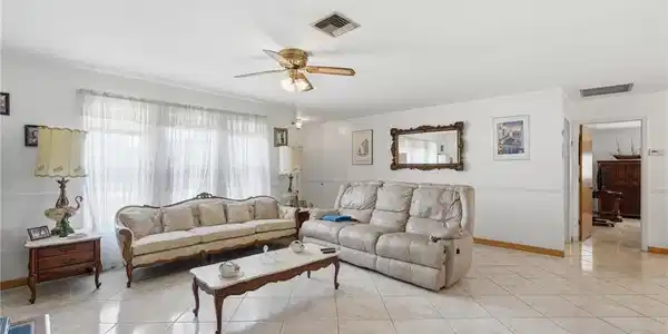 Image 2: Spacious living area featuring large format tile flooring, a wide window with sheer coverings, and a ceiling fan with integrated lighting