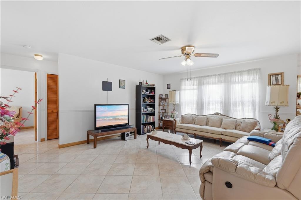 Image 3: Spacious living area featuring large windows with sheer coverings, ceiling fan with integrated lighting, and tile flooring throughout