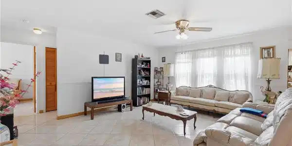 Image 3: Spacious living area featuring large windows with sheer coverings, ceiling fan with integrated lighting, and tile flooring throughout
