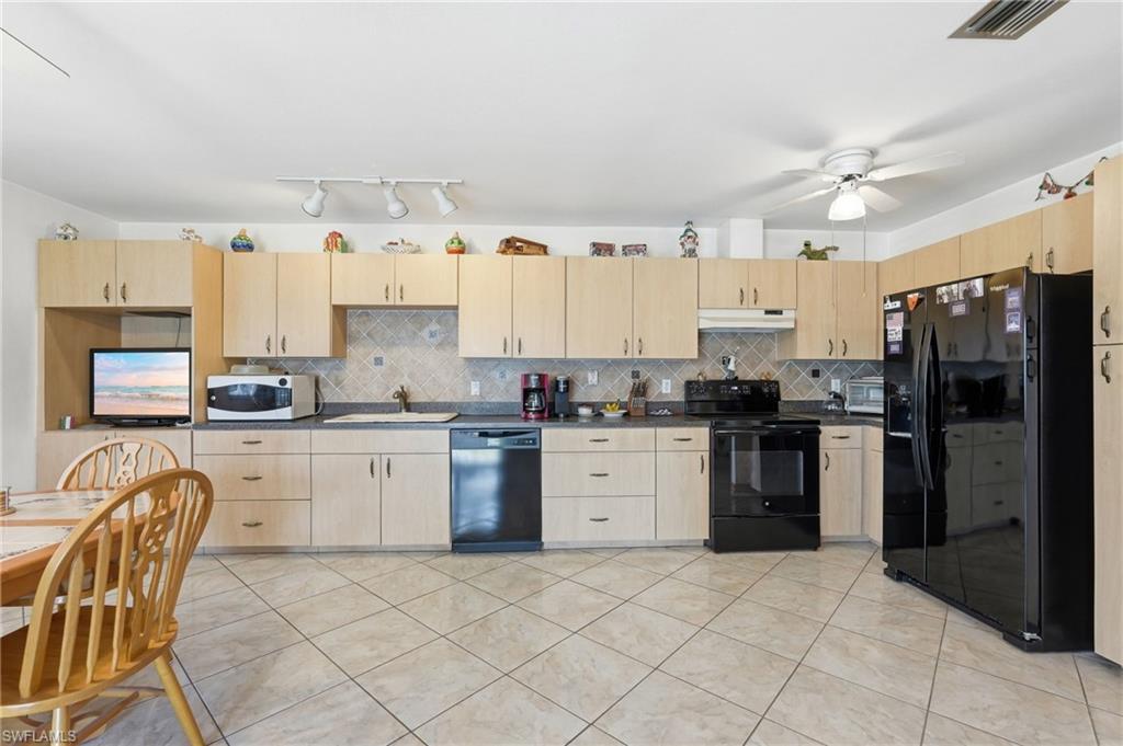 Image 4: Kitchen featuring light wood-finish cabinetry, black appliances, solid surface countertops, and a tiled backsplash