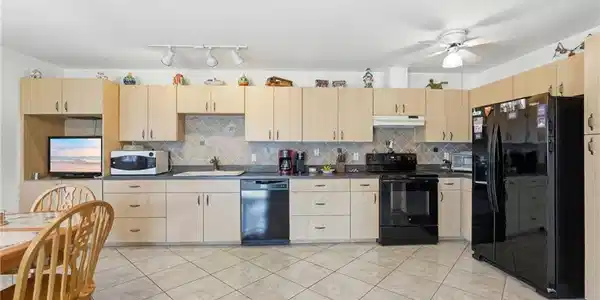 Image 4: Kitchen featuring light wood-finish cabinetry, black appliances, solid surface countertops, and a tiled backsplash