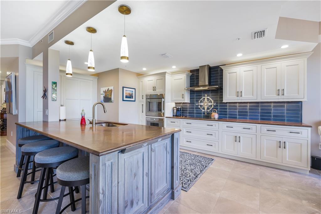 Image 1: Kitchen featuring tasteful backsplash, wall chimney range hood, a kitchen bar, white cabinets, and hanging light fixtures