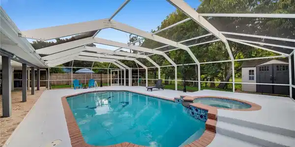 Image 2: Screened outdoor living area featuring a swimming pool, integrated hot tub, and a spacious pool deck