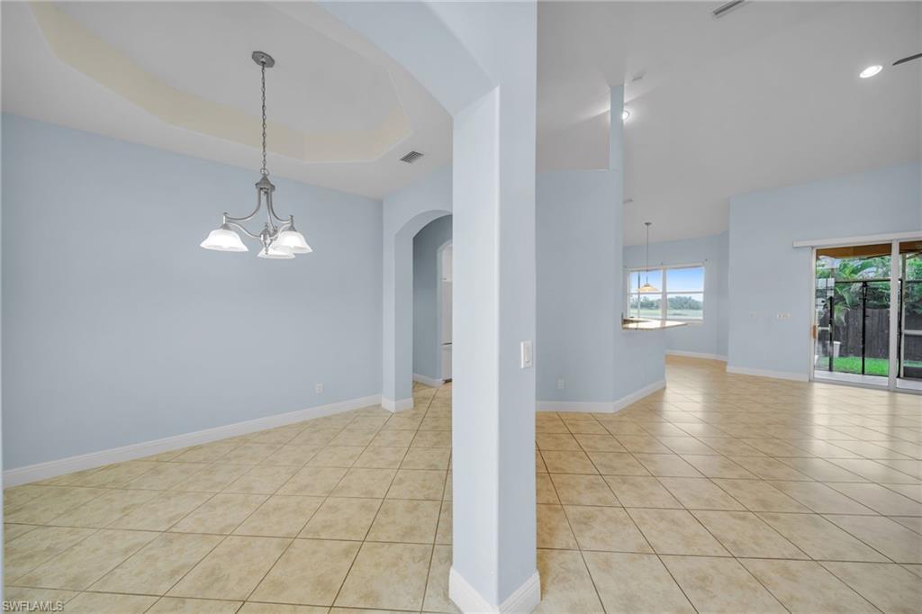 Image 3: Unfurnished room with a chandelier, light tile patterned flooring, arched walkways, and a tray ceiling