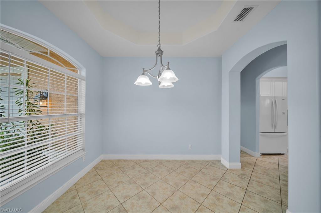 Image 4: Unfurnished room with arched walkways, light tile patterned floors, a raised ceiling, and a chandelier