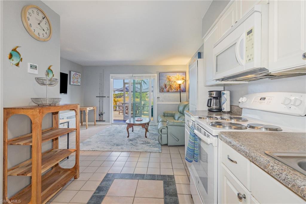 Image 4: Kitchen with white appliances, white cabinets, light tile patterned flooring, and inlaid floor details